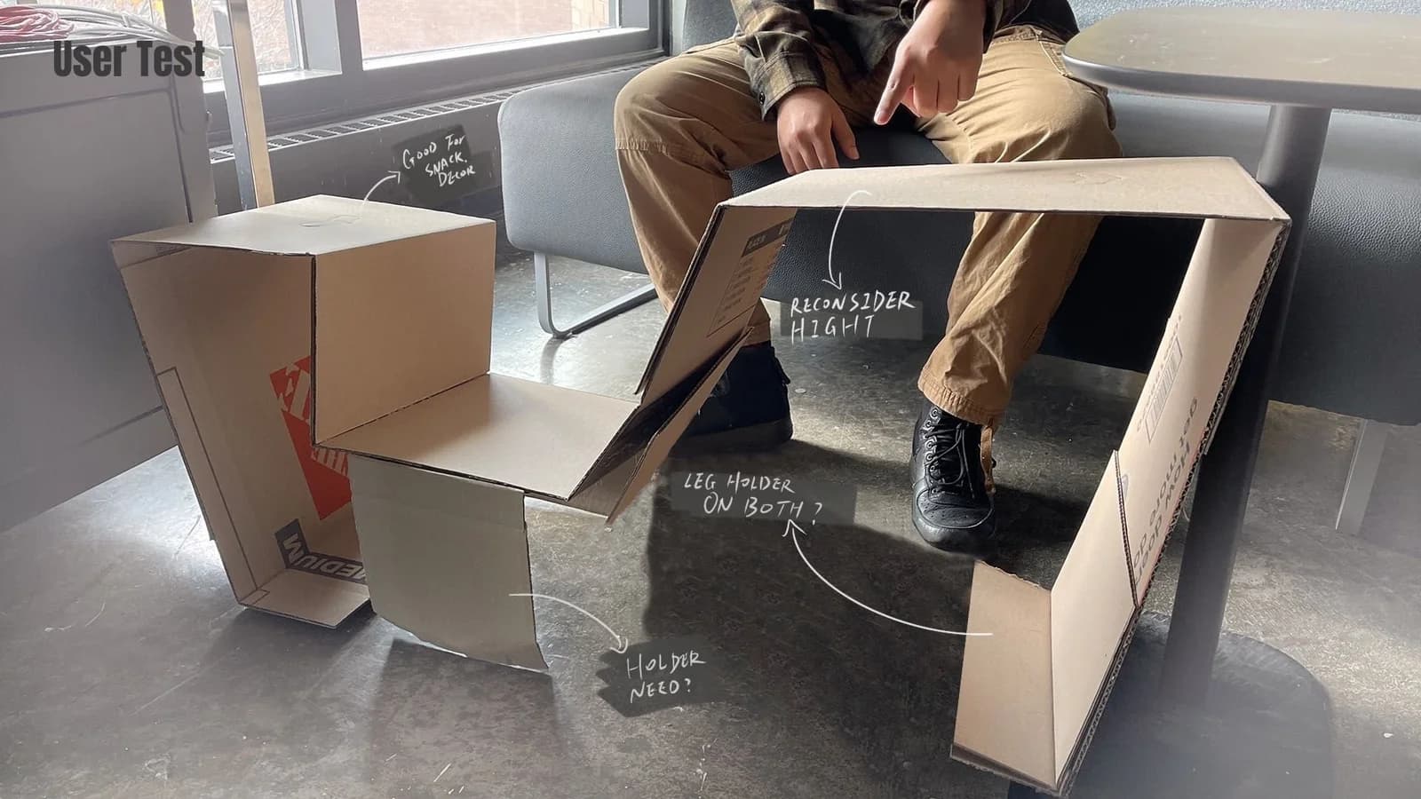 Second cardboard mockup photograph with annotations questioning the height and showing leg positions and support needs.