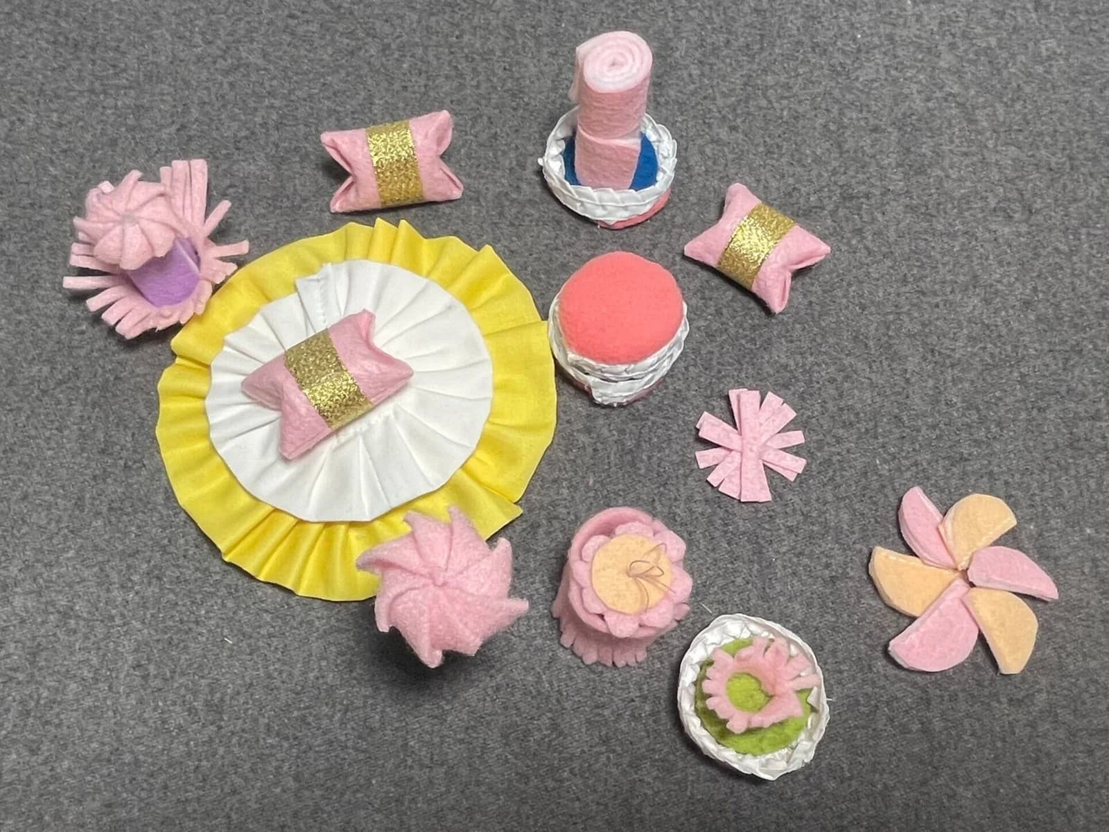 Pink, yellow and white fabric decorations, layered desserts and a cake surface laid out on grey fabric.