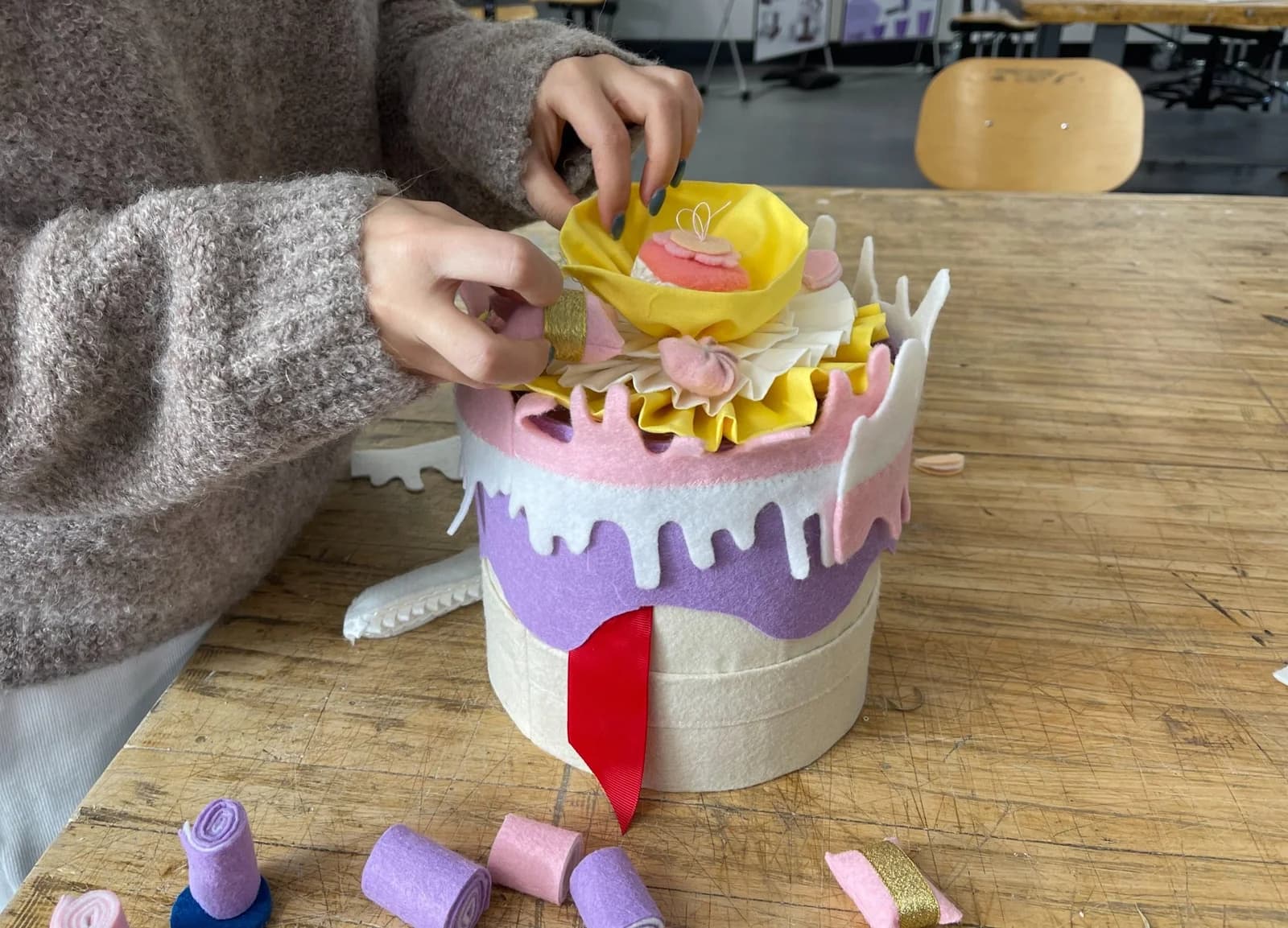 Hands adding a yellow fabric layer to a purple and white cake-shaped soft toy.