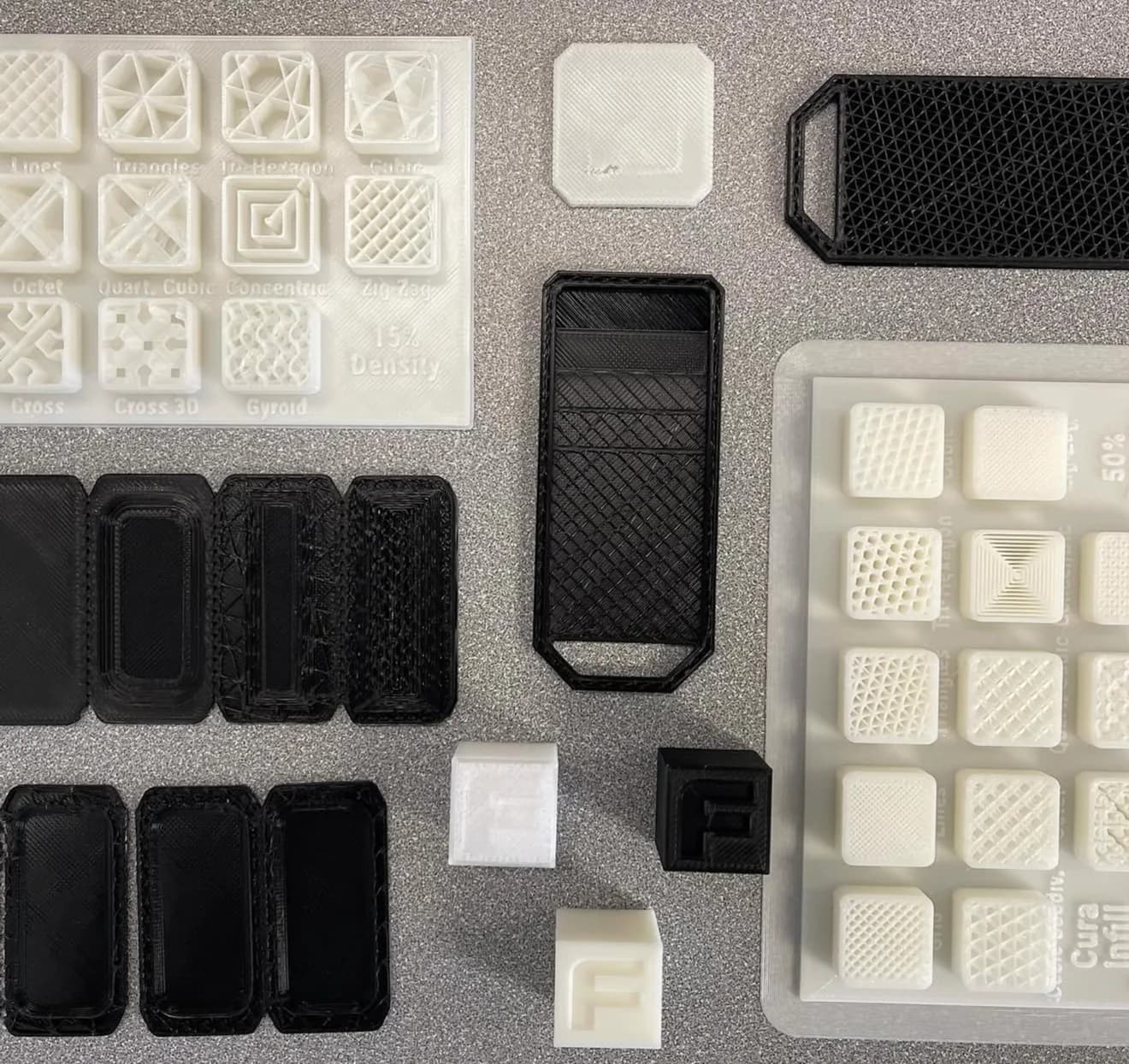 Black and white printed objects, including patterned tiles, compartmented trays and handled forms, are arranged on a grey surface.