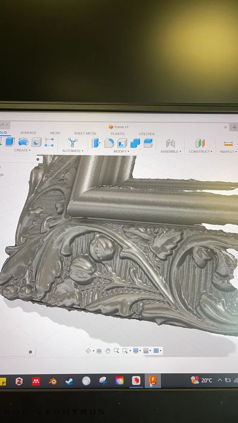 A laptop screen shows a grey digital model of an ornate frame corner with leaf and scroll relief.
