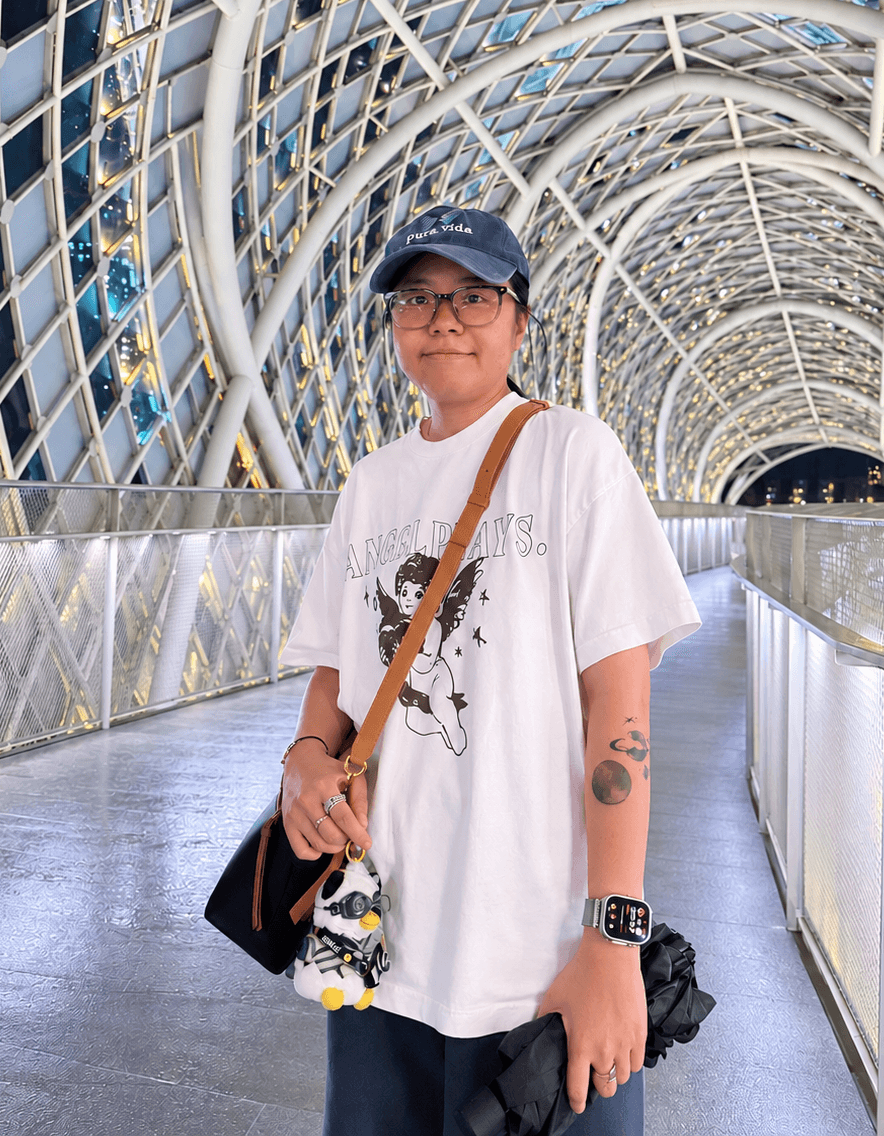 Xinxin Li standing in a glass-covered walkway beneath curved structural beams.